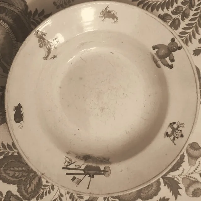 Un plato antiguo de loza, con dibujos de un conejo, un oso de peluche y un ratón en el borde